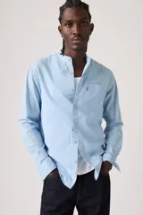 Camisa celeste de manga larga con cuello mao y cierre frontal de botones. Cuenta con un bolsillo aplicado en el pecho adornado con una pequeña etiqueta roja.