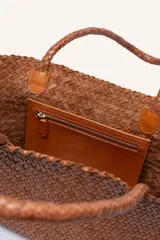 Bolso tipo tote de cuero vacuno, completamente trenzado a mano. El color es marrón oscuro, casi chocolate. Posee dos asas de hombro trenzadas.