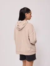 Canguro Rusty con capucha y efecto lavado color beige, de corte oversize, con bolsillo tipo canguro frontal, cordones ajustables y parche de la marca en el pecho. Presenta costuras expuestas y detalles deshilachados.