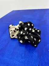 Colita de pelo tipo scrunchie de tela negra con estampado de lunares blancos.