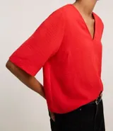 Blusa Cortelle de corte holgado confeccionada en crepé, con escote en V delantero y trasero, y mangas cortas. Presenta una tira decorativa entre los hombros en la espalda.