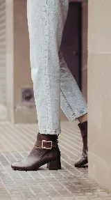 Bota corta de cuero color chocolate, con diseño minimalista, taco cuadrado de 4 cm y una hebilla metálica decorativa en el tobillo sobre una banda de gamuza.