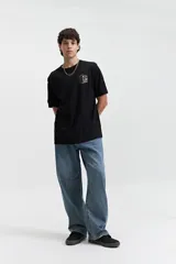 Remera negra de manga corta con cuello redondo y fit regular. Presenta un estampado frontal con gráficos circulares y texto en blanco y naranja.