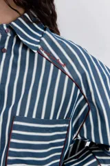 Camisa de manga larga a rayas verticales azul marino y blancas, con cuello clásico, bolsillo de parche en el pecho y ribetes finos en color rojo.