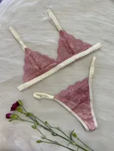 Conjunto de lencería compuesto por un corpiño triangular de encaje y una bombacha tipo tanga a juego. Ambas piezas presentan encaje en tono rosado con detalles de terminaciones en color crema.