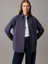 Camisa azul marino de popelín de algodón, corte holgado, cuello en punta, manga larga con puños abotonados, bolsillo de parche en el pecho e insignia con el monograma de Calvin Klein en el bolsillo del pecho.