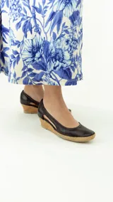 Zapato de cuero negro con taco corrido revestido en corcho y plataforma de yute trenzado. Cuenta con diseño lateral abierto y puntera redondeada.