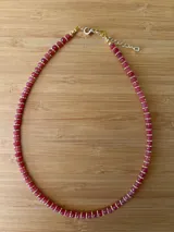 Gargantilla de cuentas facetadas color fucsia, separadas por pequeñas cuentas doradas. Cierre de mosquetón dorado con cadena de alargue.