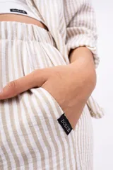 Pantalón largo de mujer, de corte amplio y tiro alto, con estampado a rayas verticales en tonos beige y blanco. Tiene cintura elástica con cordón ajustable.