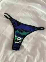 Bombacha tipo colaless con estampado abstracto en tonos azules, verdes y negros, con bordes y tiras laterales ajustables en color negro.