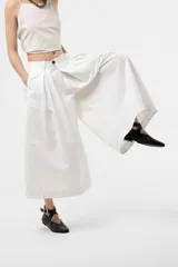 Pantalón wide leg de color blanco, de silueta amplia y gran movimiento, con pliegues delanteros que aportan volumen y estructura, y cintura definida.