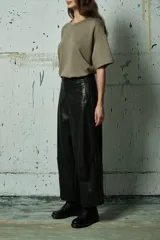 Pantalón de cuero sintético negro de corte ancho y tiro alto, con costuras verticales decorativas en el frente y cierre frontal con botón.