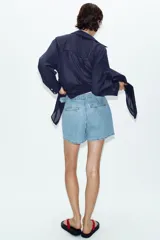 Falda pantalón cruzada de denim en color celeste, con diseño cruzado al frente, cierre frontal oculto y hebilla decorativa redonda en la cintura.
