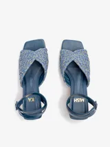 Sandalias de tacón medio en color azul, con capellada de rafia labrada en tonos azules y dorados, pulsera de cuero nobuck enlazada al tobillo con cierre de hebilla, y taco de madera natural lustrada de forma cilíndrica. Cuenta con puntera cuadrada.