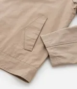 Campera de sarga color beige con cuello inglés, cierre frontal de cremallera, mangas largas y bolsillos laterales. Diseño minimalista y versátil con forro interior.