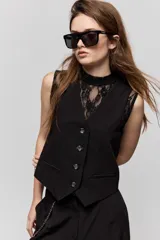 Chaleco sastrero negro de escote en V, con cierre frontal de botones y bolsillos ribeteados simulados. Presenta terminación en punta en el delantero y diseño entallado de inspiración tailoring.
