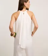 Mono largo blanco de crepé, con cuello halter, sin mangas y superposición fruncida en el tronco. Se ata con lazo en la nuca.