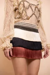 Falda corta de Patbo modelo Rita Fringe, diseño de tres niveles con flecos en tonos beige, negro y marrón, y cintura con detalles tejidos.
