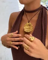 Collar artesanal con dije central de metal con textura orgánica irregular que evoca una ostra. El dije está montado sobre un cordón de algodón natural, permitiendo un uso versátil y regulable.