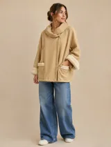 Chaquetón de paño color beige con cuello envolvente, cierre de botones en el cuello, mangas anchas con puños de piel sintética y bolsillos frontales con detalles de piel sintética.