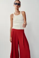 Pantalón fluido de tiro alto en color blanco, con pinzas delanteras, cintura elástica en la espalda y perneras anchas con aberturas laterales pronunciadas.