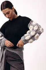 Sweater de punto con cuerpo liso en color negro y mangas largas tejidas en crochet gris con aplicaciones de flores en relieve color blanco.