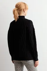 Polerón de punto negro con cuello alto y diseño de trenzas verticales en el frente. Posee mangas largas con puños acanalados y un corte holgado.