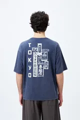 Remera negra de corte amplio con mangas cortas y cuello redondo. Presenta un pequeño estampado rectangular en el pecho y un estampado grande en la espalda con motivos japoneses.