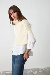 Capita de punto color crudo, con cuello alto vuelto y diseño amplio y corto.