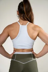 Top deportivo blanco con cuello halter y logo de la marca en el frente.