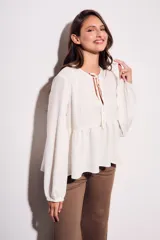 Blusa color crudo de viscosa y lino con bordados en el frente, escote con lazo y mangas largas. Corte holgado con frunce en la cintura.