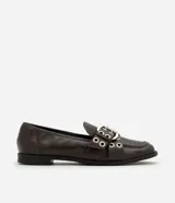 Mocasín Satinato de poliuretano color marrón oscuro, con punta redondeada, tacón bajo y empeine decorado con tiras cruzadas, hebilla ajustable y ojetes metálicos.