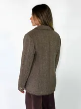 Blazer de corte clásico con textura de tejido de punto, color beige con detalles moteados. Presenta solapas tradicionales, cierre frontal de un botón, bolsillos laterales con solapa y bordes con acabado desflecado.
