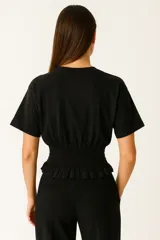 Remera blanca de algodón con cuello redondo, manga corta y sección inferior con smock elástico que ajusta la prenda al cuerpo y crea un pequeño volante en el ruedo.