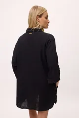 Vestido camisero negro de algodón, con mangas tres cuartos y cuello camisero. Presenta detalles de costura en zigzag color naranja en el cuello y en los puños.