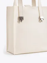 Cartera tipo tote pequeña de cuero color tostado, con doble asa superior y herrajes metálicos plateados en forma de llama en la base de las manijas. Presenta el logo de la marca estampado en la parte inferior frontal.