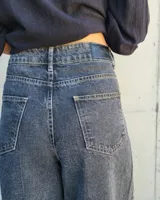 Pantalón de jean color beige, de corte recto y tiro alto, con ruedo deshilachado y cierre frontal con botón y cremallera.