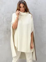 Poncho de lana color crema con cuello alto y aberturas laterales, con bordes en contraste de color marrón.