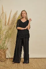 Conjunto de dos piezas color negro, compuesto por una blusa de mangas cortas con superposiciones y volados, y un pantalón holgado de corte ancho.