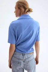 Remera de punto suave de algodón, color celeste, con hombros caídos, mangas cortas y detalle de cuello tipo fular con lazo integrado.