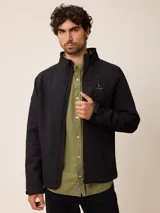 Campera softshell negra con cierre frontal completo, cuello alto y bolsillos laterales con cierre. Presenta un bolsillo adicional en el pecho con cierre y el logo de la marca bordado.