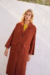 Abrigo oversize color ladrillo, confeccionado en lino pesado, con botonadura simple, bolsillos con solapa y ventilación trasera.