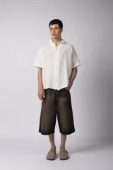 Camisa de manga corta confeccionada en lino, de corte relajado y cuello clásico. Presenta un diseño minimalista en color blanco con textura natural.