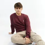 Buzo de punto color bordó, de corte clásico y manga larga. Presenta un pequeño logo bordado en el pecho.