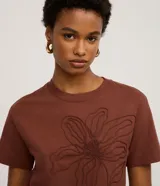 Remera de manga corta color marrón, con cuello redondo y corte recto. Presenta un bordado grande en relieve de una flor en el centro del pecho.