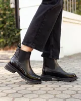 Botinetas tipo Chelsea de cuero negro, con paneles laterales elásticos y suela track dentada de goma. Presentan una combinación de texturas entre cuero mate y cuero charolado en la puntera y el talón.