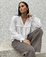 Camisa blanca de corte amplio con escote en V, canesú delantero con bordado floral y detalle de volado pequeño. Presenta mangas largas con puños elastizados y cierre frontal de botones.