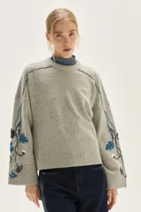 Sweater de punto color gris con cuello redondo, mangas amplias y diseño floral bordado a mano en las mangas.