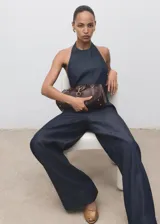 Mono largo de denim oscuro con cuello halter y espalda descubierta. Presenta un diseño de corte recto y holgado con bolsillos laterales y cierre de cremallera en la parte posterior.