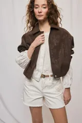 Campera marrón de poliuretano con acabado texturizado, silueta relajada, cuello camisero, cierre frontal, hombros caídos y mangas amplias con efecto abombado.